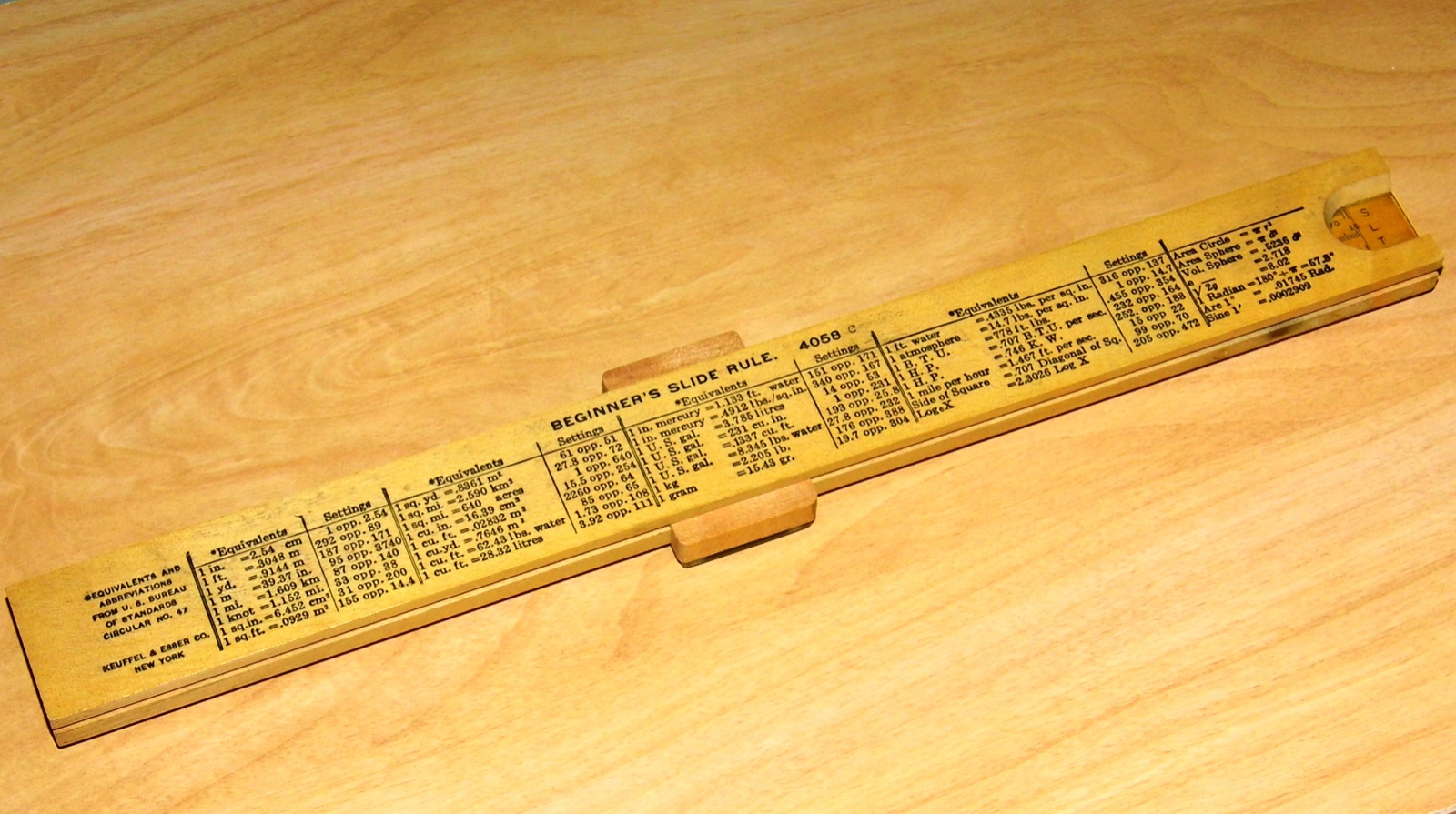 Keuffel &amp; Esser "Beginner's Slide Rule" (reverse side), model 4058C, wood-framed cursor, made in USA, circa 1930s. This is the underside of a low-cost slide rule intended for students and other beginners, with its scales printed directly on wood rather than engraved into celluloid facing. It is a basic "Mannheim-type" slide rule, with two single-decade (1-to-10) scales C and D for ordinary multiplication and division, and two two-decade (1-to-100) scales A and B for calculations involving squares and square roots. This is a view of the rule's underside, which has an extensive table of equivalents. On the right end is a transparent notch with hairline; this shows the back side of the removable, reversible slide, with its sine (S), tangent (T), and logarithm (L) scales.)